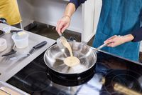 A person pours crepe batter into the All-Clad D3 Stainless-Steel 12-Inch Fry Pan