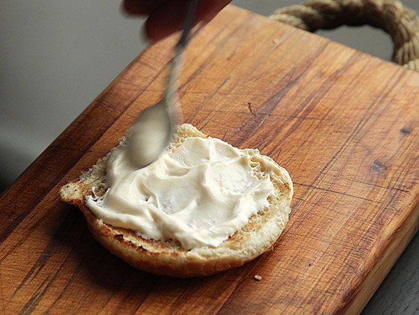 Half of a toasted bun being slathered in a generous quantity of mayonnaise.