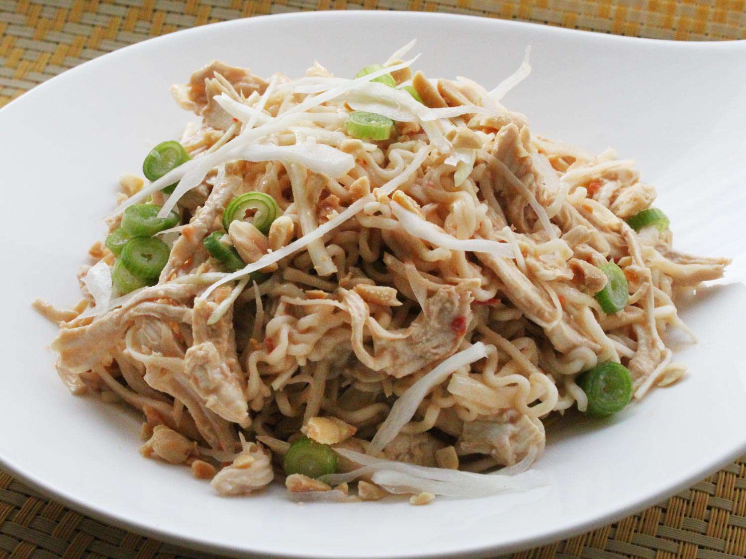 A plate of cold sesame noodles topped with shredded chicken, cabbage, and toasted peanuts