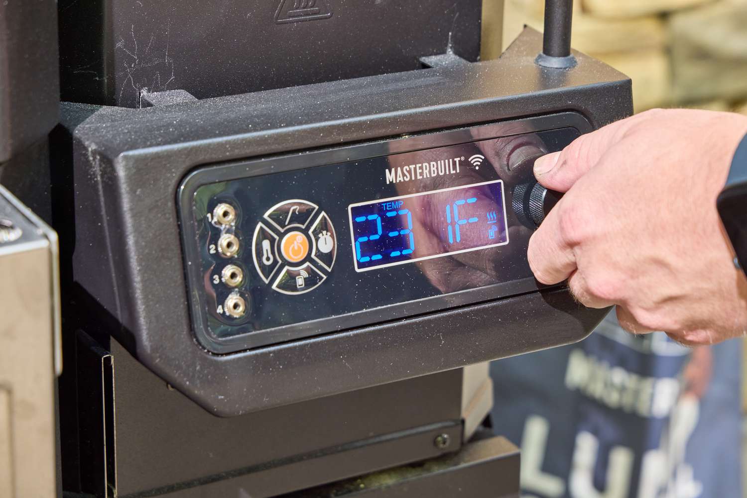 A person turns a dial on the Masterbuilt Gravity Series 1150 Digital Charcoal Grill and Smoker