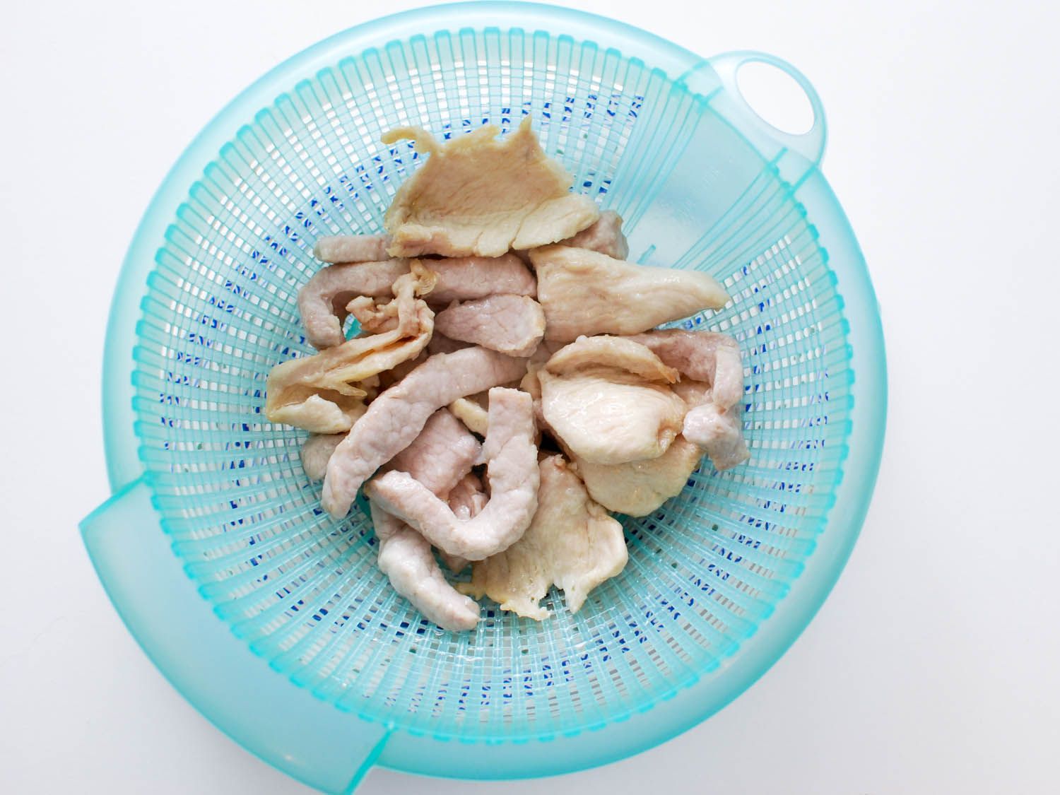 Water-velveted chicken and pork resting in a light blue strainer.