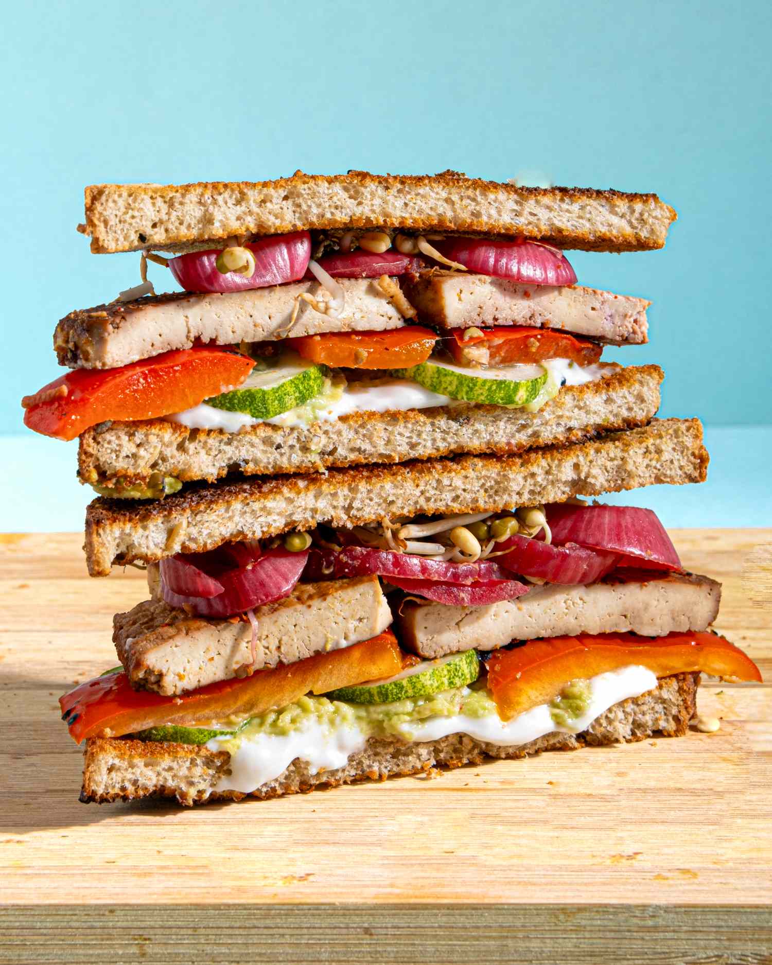 Stacked sandwiches with tofu onions cucumber and red peppers on a wooden surface