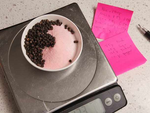 The ingredients for the the cure being weighed on a digital scale. Several sticky notes are visible with gram weight calculations scrawled on them.