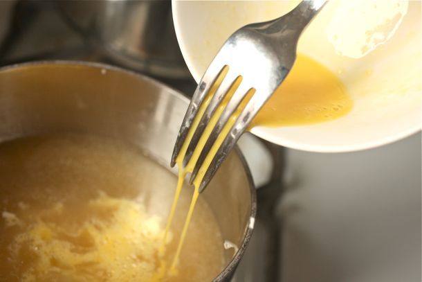Using a fork to drizzle the whisked eggs and cornstarch slurry into egg drop soup.