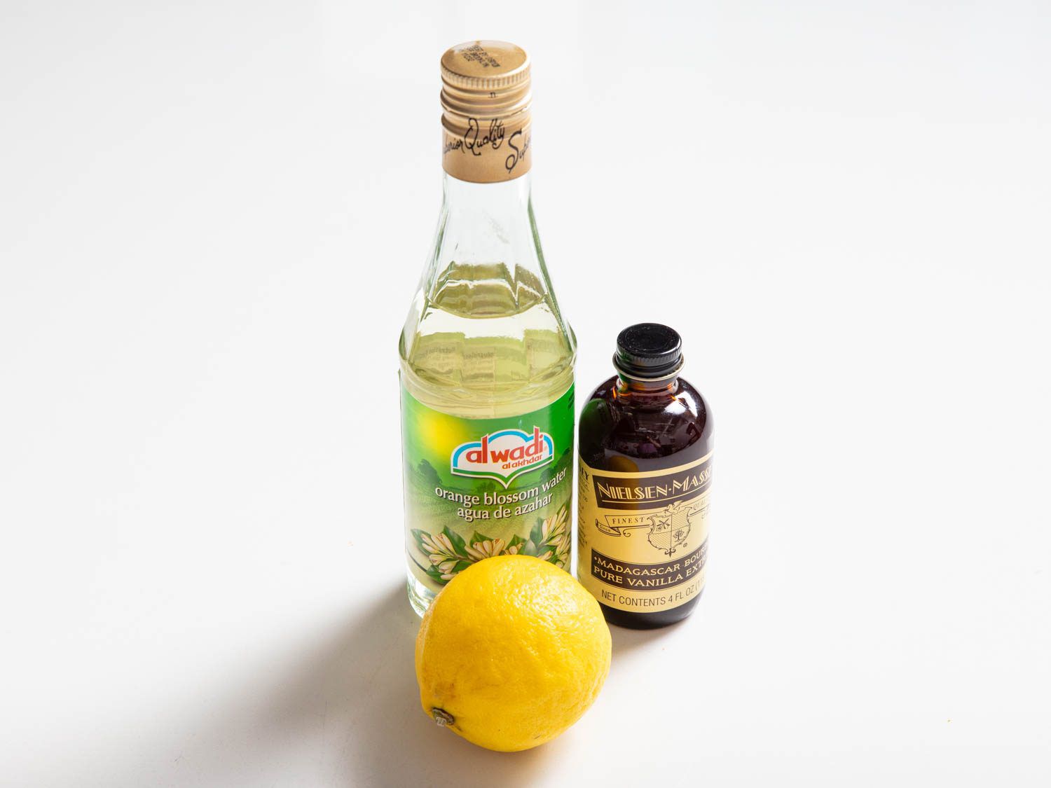 A trio of aromatics: a bottle of orange flower water, a lemon, and a bottle of vanilla extract.