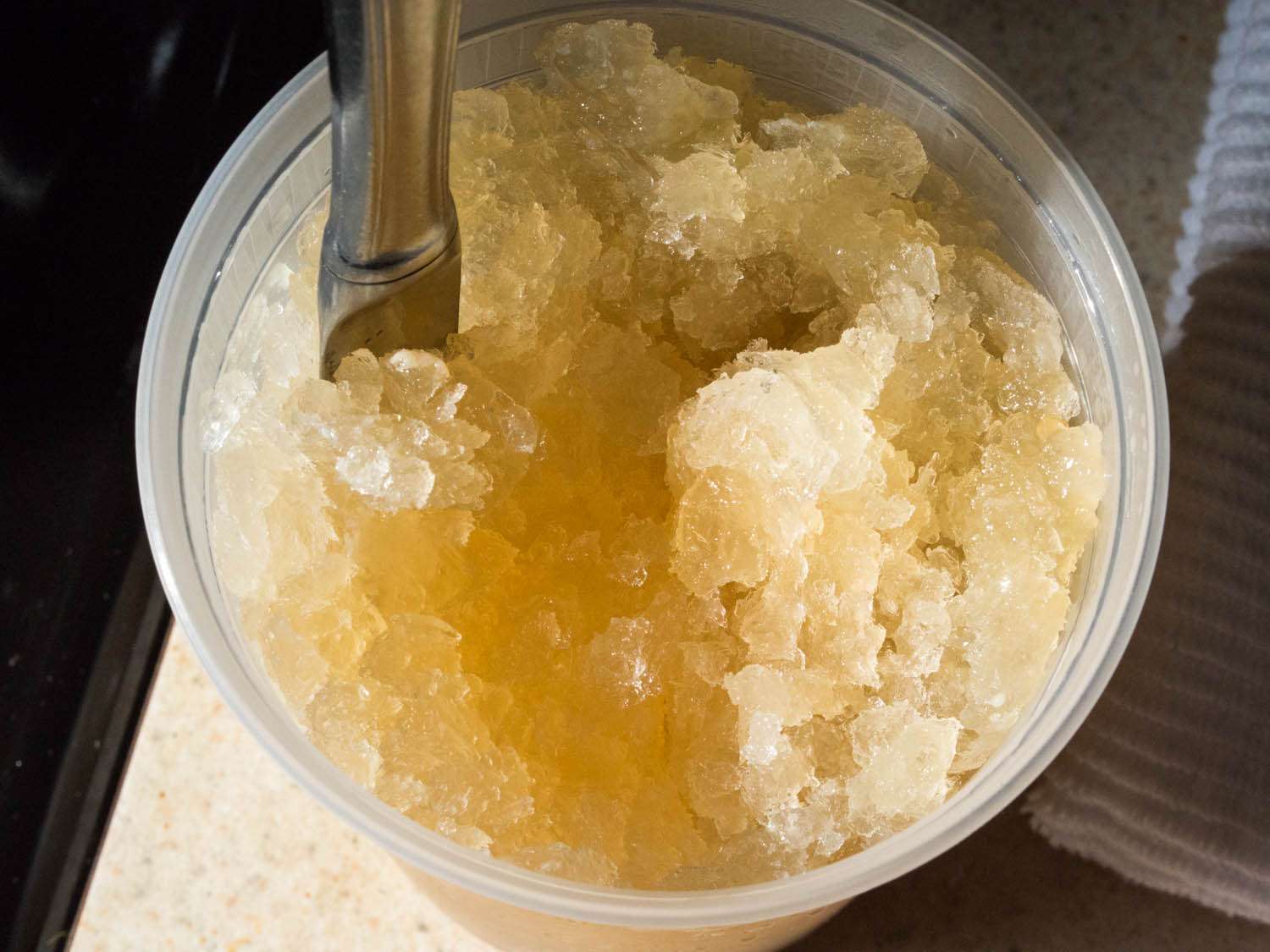 A plastic quart container holding a mix of frozen chicken stock and gelatin. The stock has broken up in a way where it is visually granular, indicating it has the right texture.