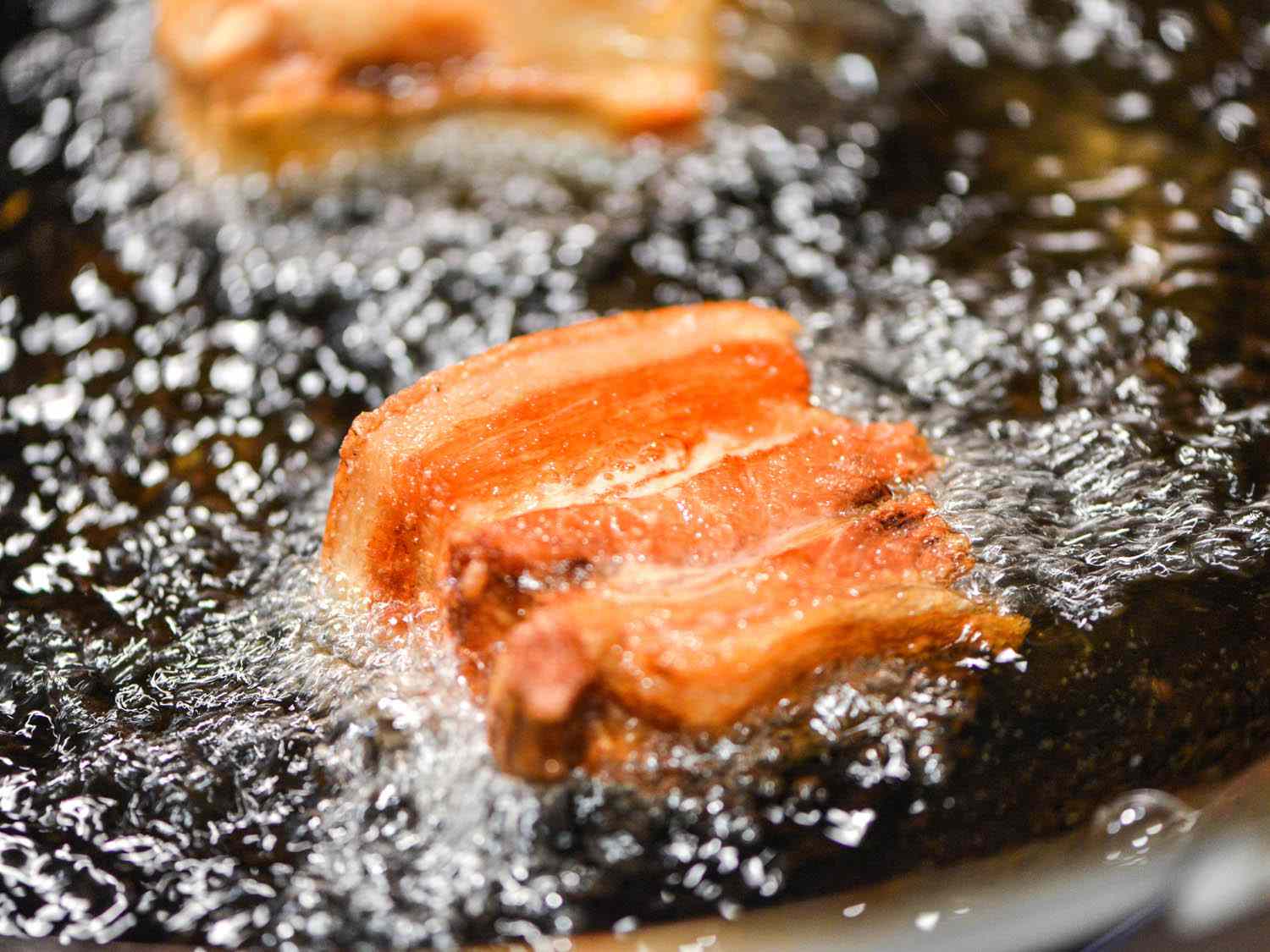 Cuts of lechon kawali being fried in bubbling oil.