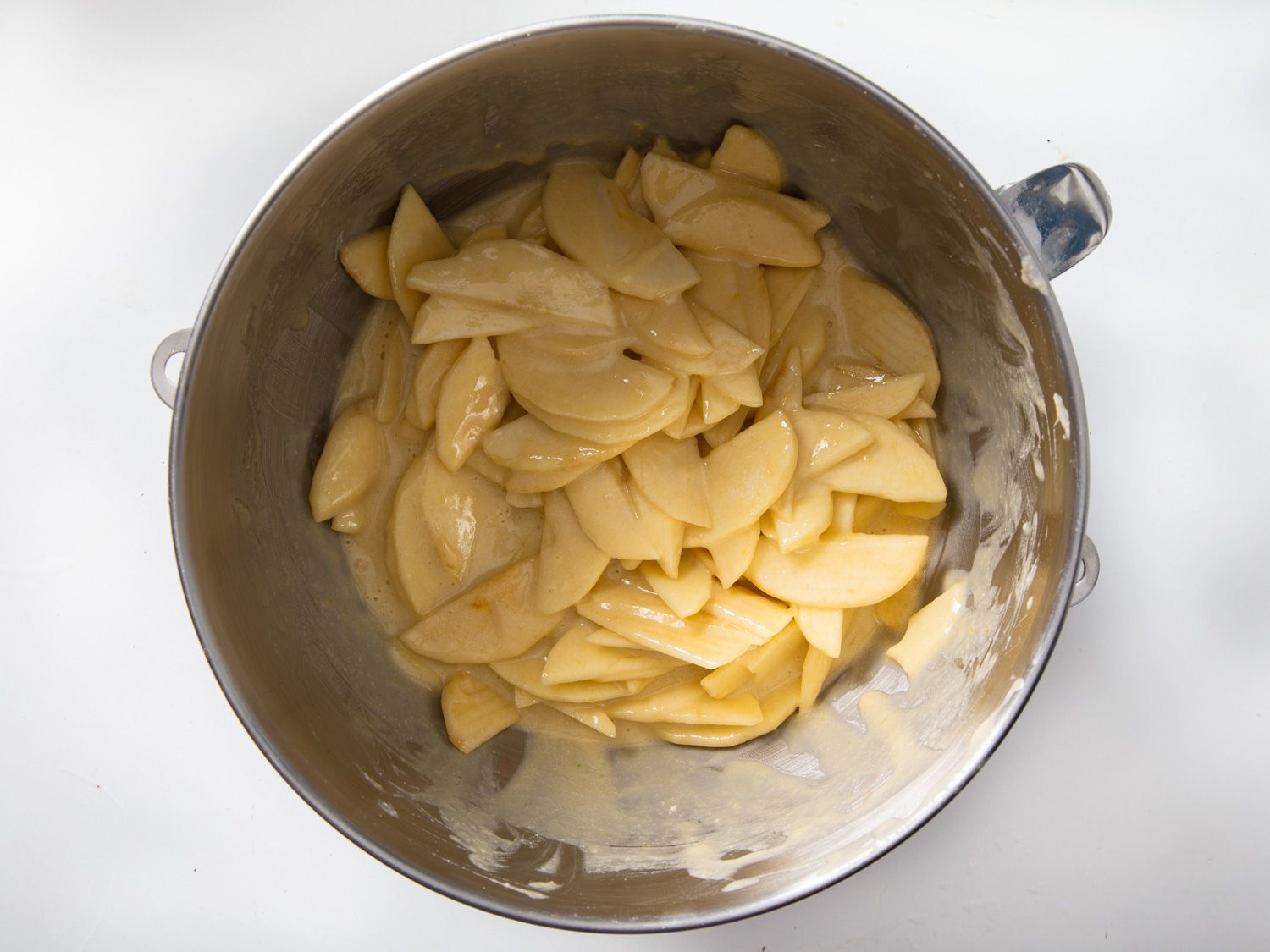 A large mixing bowl filled with thinly sliced apples coated in a custardy batter.