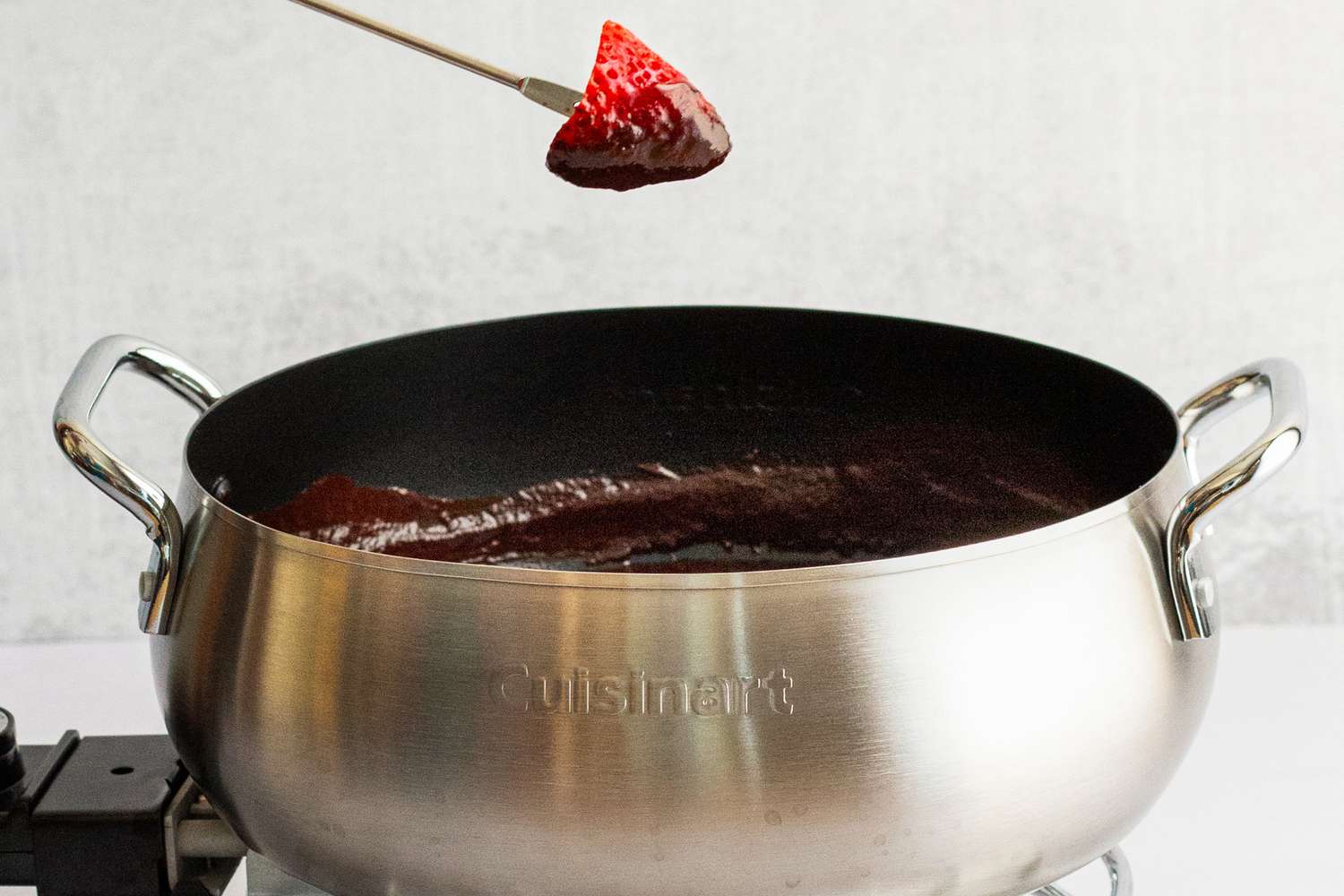 A strawberry being dipped into chocolate fondue.