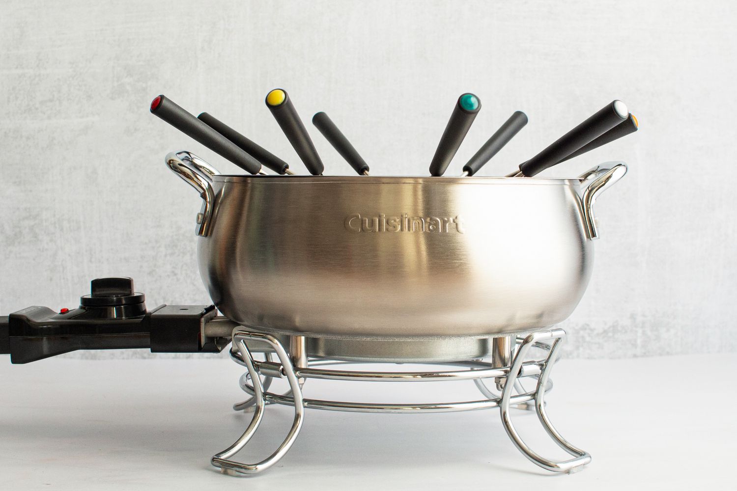 The Cuisinart electric fondue pot with fondue forks sticking out of it.