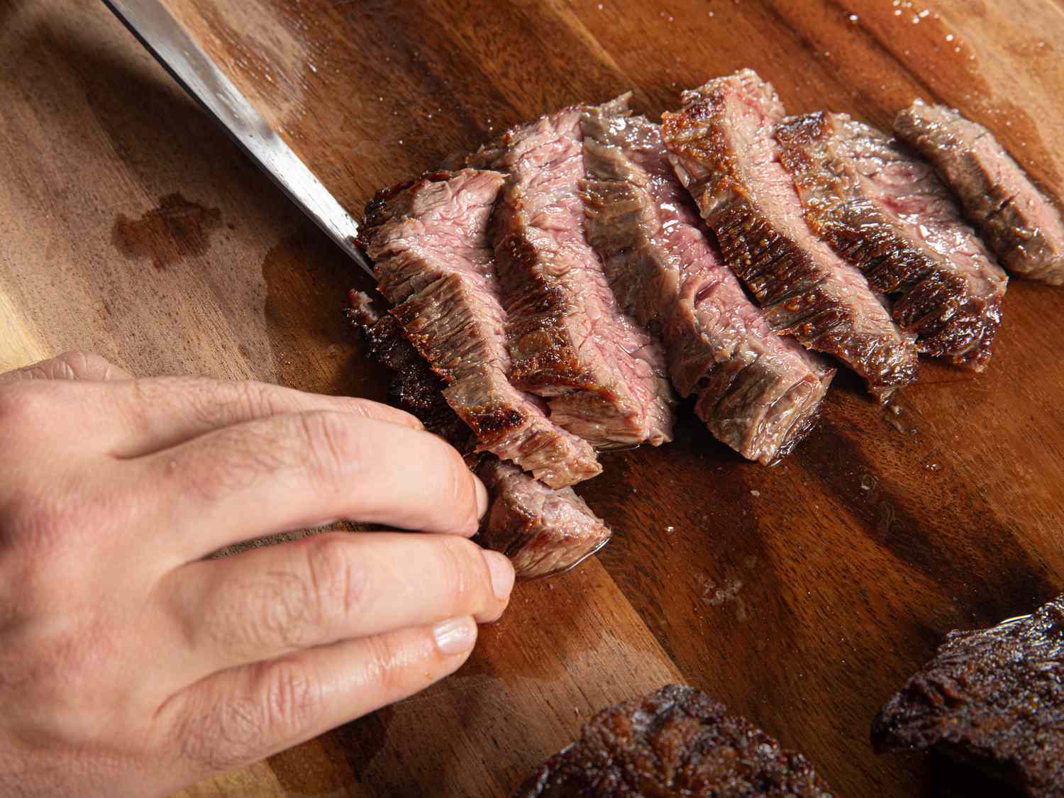 Steak being sliced on a wooden cutting board.