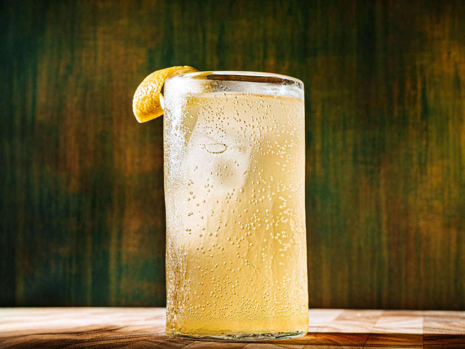A glass filled with a fizzy lightcolored beverage garnished with a lemon wedge placed on a wooden surface