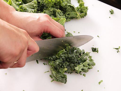 Author slicing kale leaves on a cutting board with a chef's knife.
