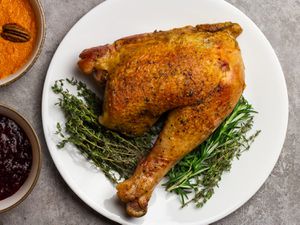 A sous vide turkey leg on a bed of herbs next to sweet potatoes and cranberry sauce.