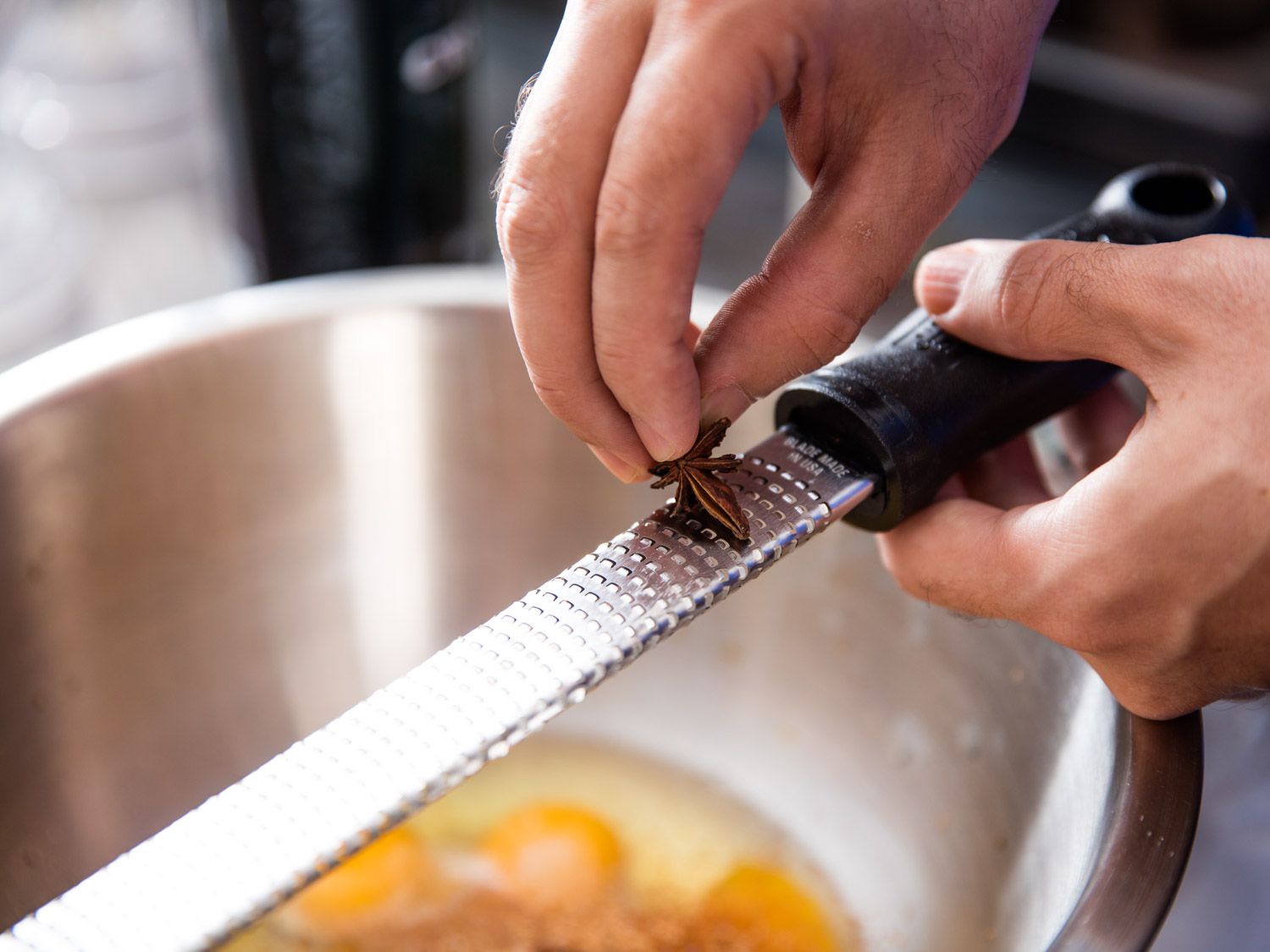 A star anise pod is grated with a microplane over a mixing bowl.