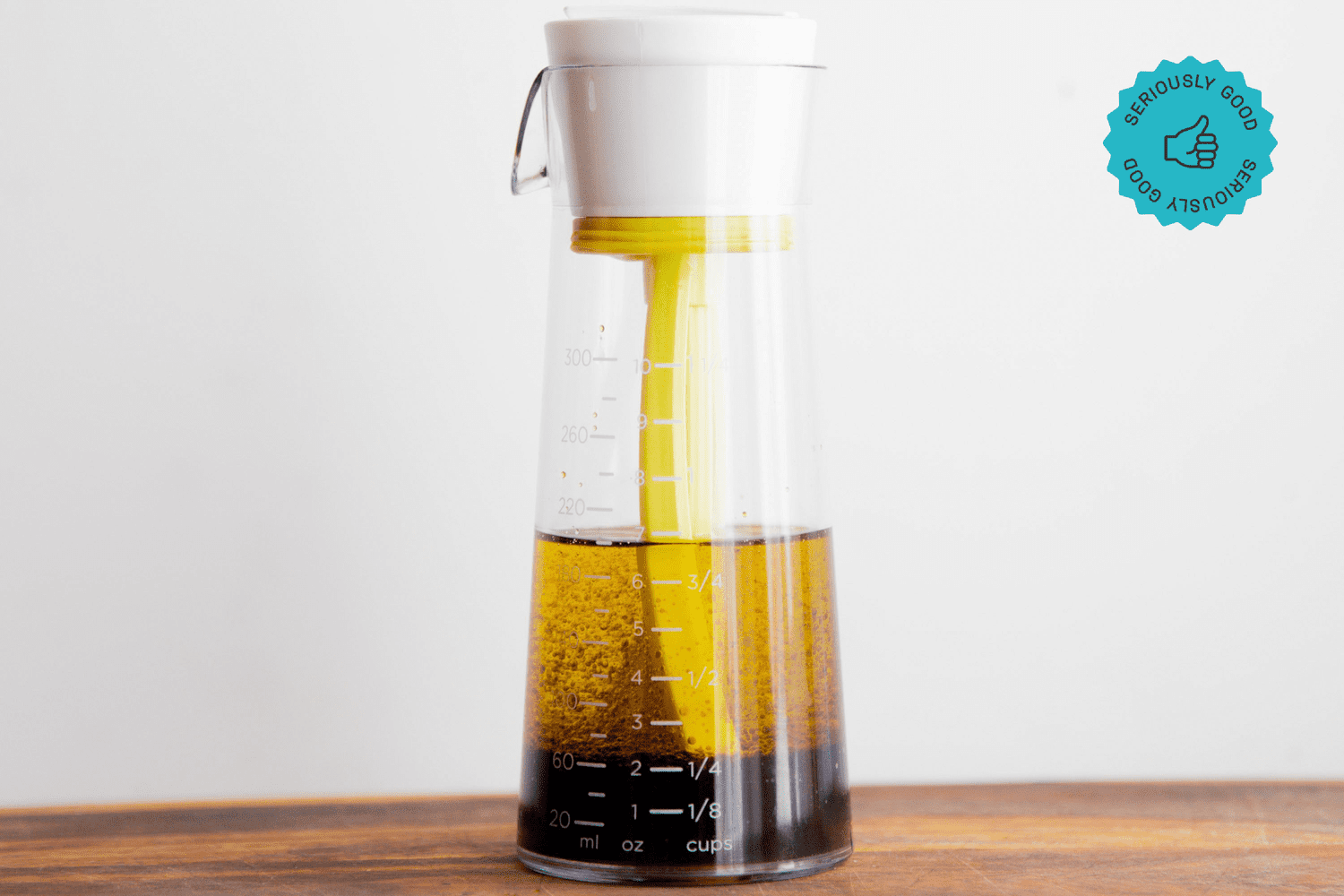 The Emulstir salad dressing mixer on a wooden table in front of a white wall.