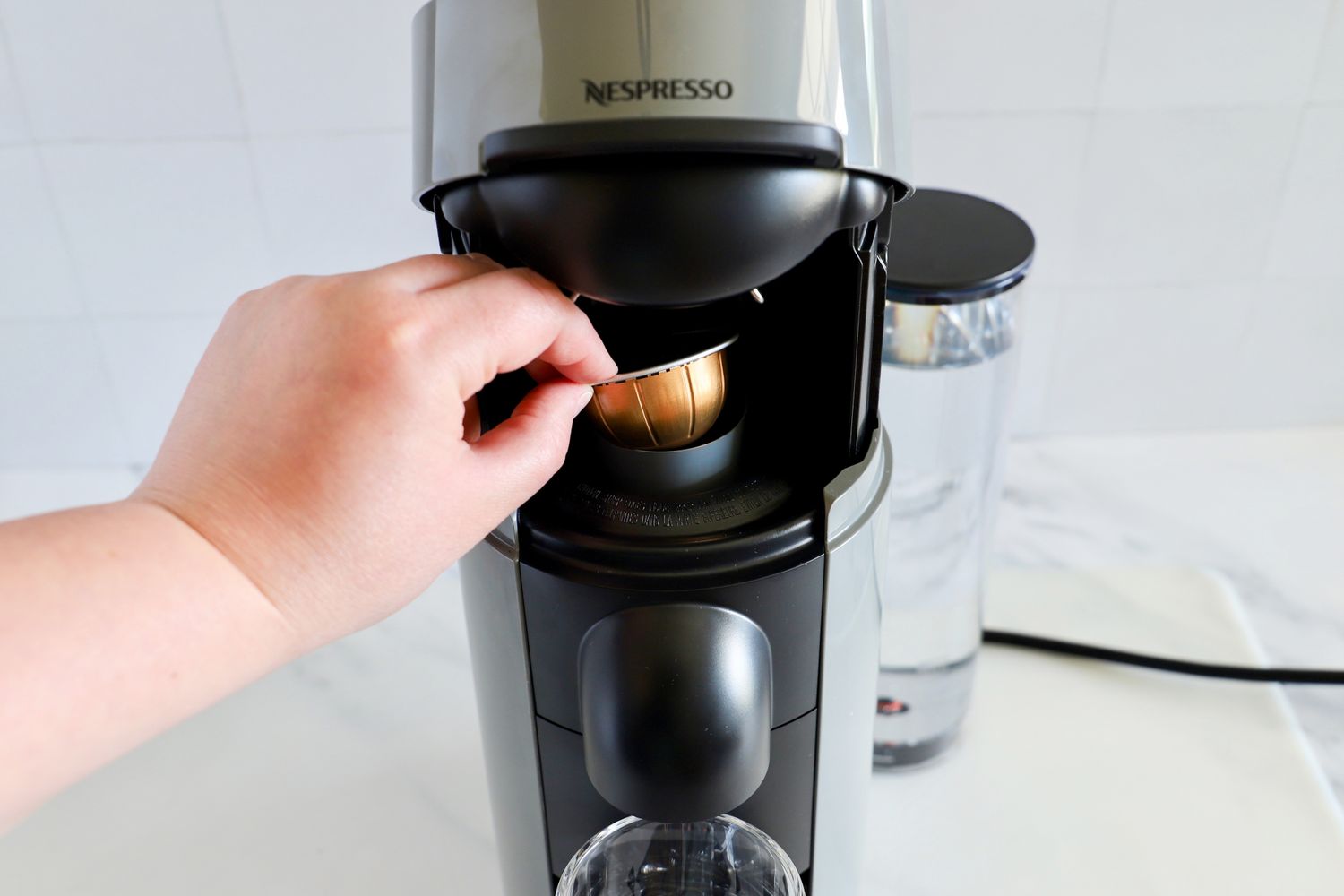 A hand placing a pod into the Nespresso VertuoPlus Coffee and Espresso Machine by De'Longhi