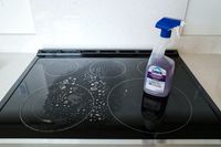 A dirty stovetop with a bottle of kitchen degreaser placed on top