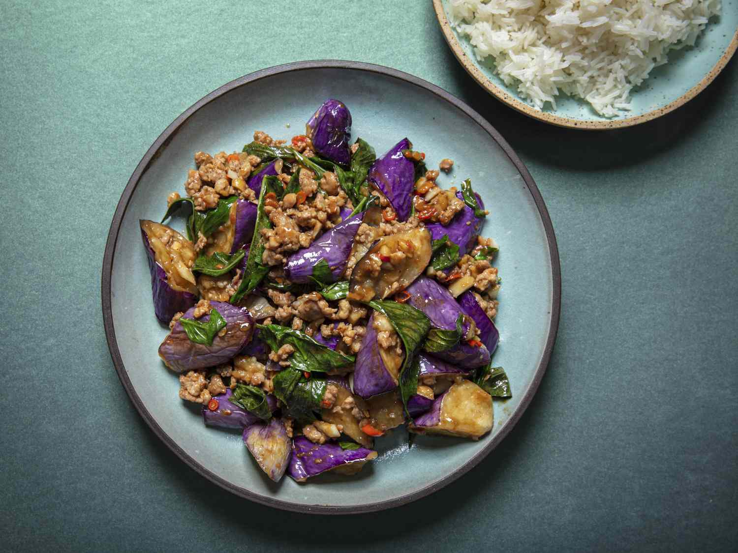 Overhead view of eggplant stir-fry plated on a blue plate on a blue background.