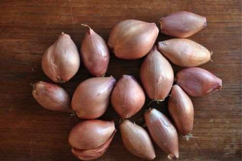 Two pounds of whole unpeeled shallots on a wood tabletop.