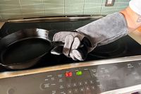 A person lifts a cast iron pan while wearing the Breeo Fire Pit Gloves