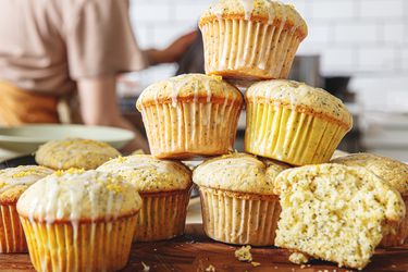 Lemon poppy seed muffins stacked on a wooden surface, with a partially sliced muffin showing the interior
