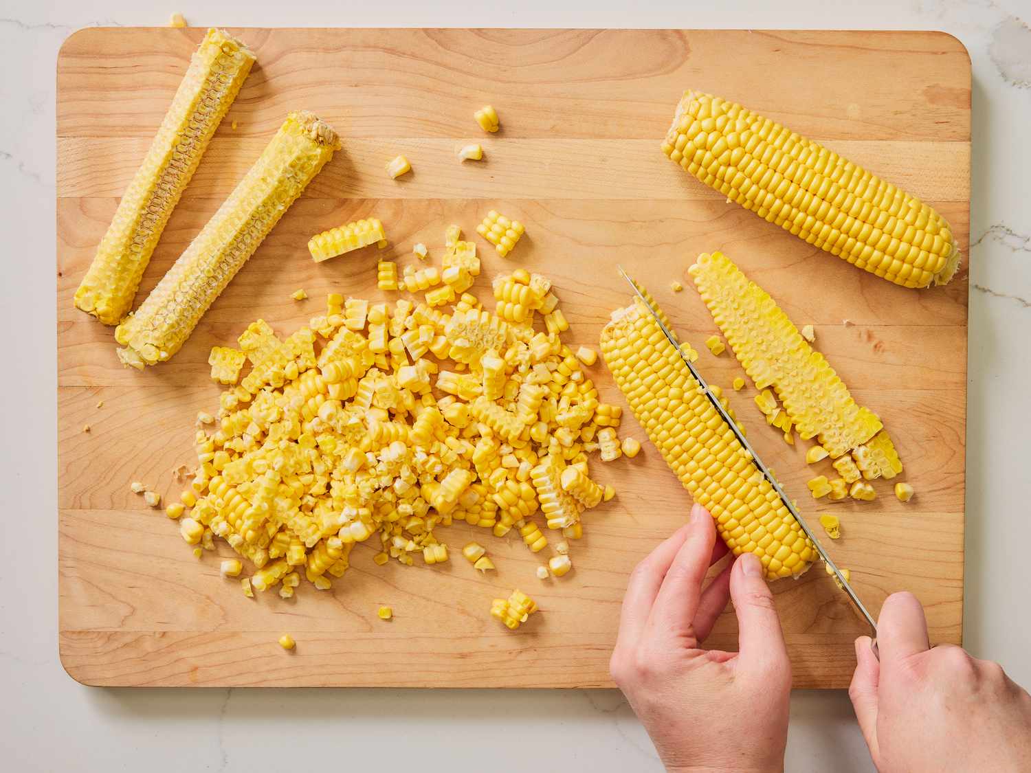 Slicing corn kernels away from corn cobs on a wooden chopping board 