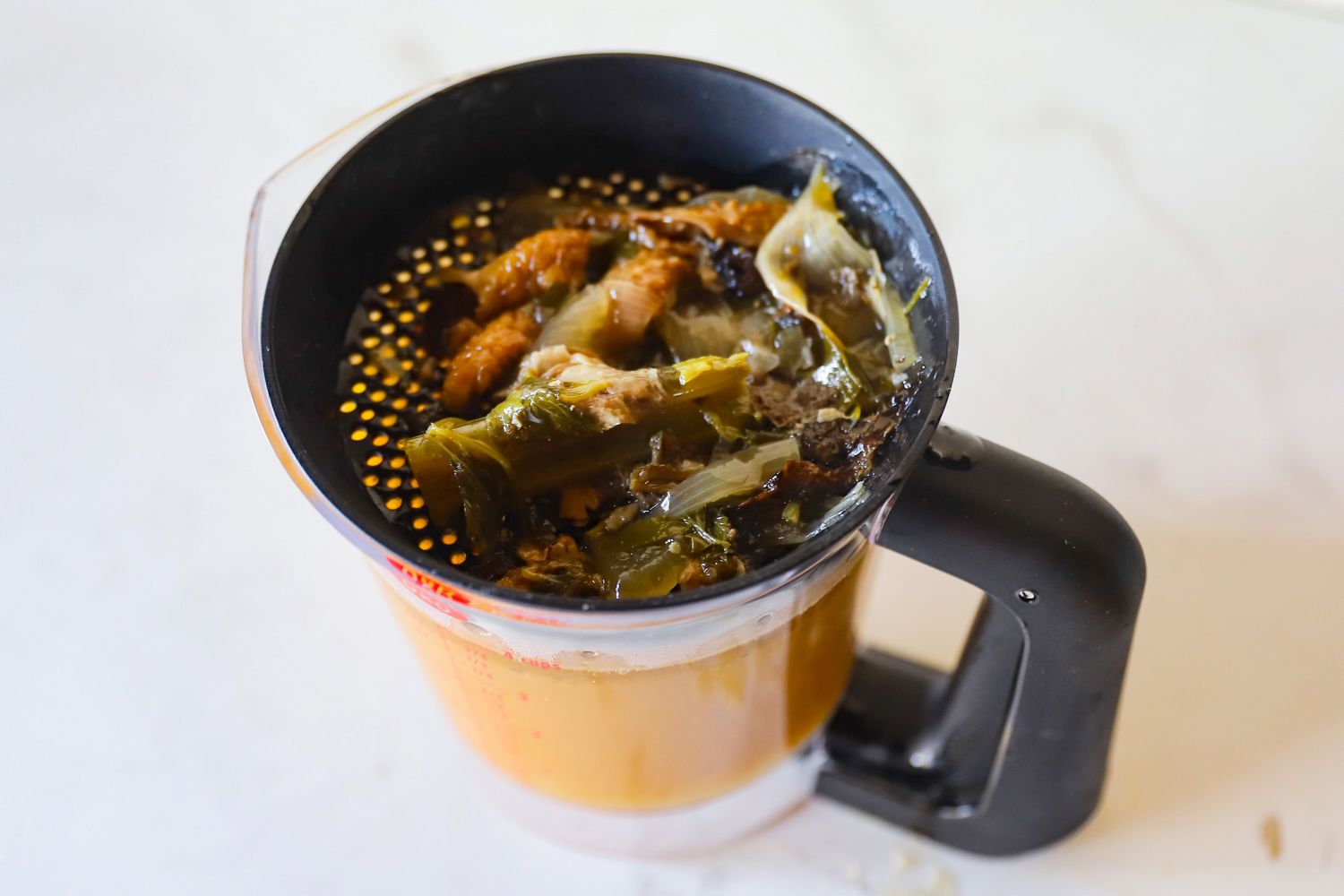 Food remnants being strained in a measuring cup with a strainer on top