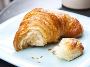 A croissant, torn open to display its interior, on a blue plate.