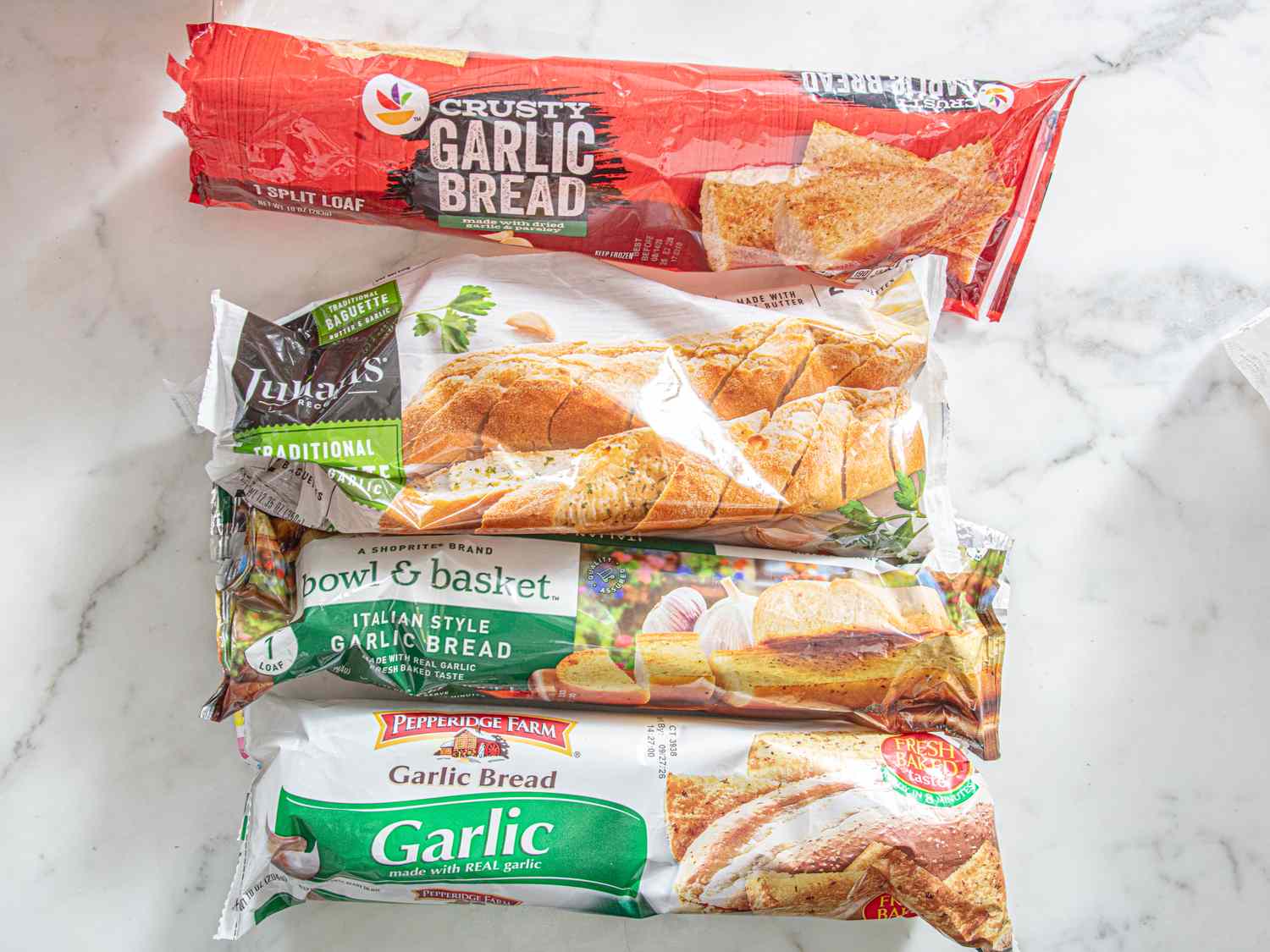 Four varieties of prepackaged garlic bread on a marble surface