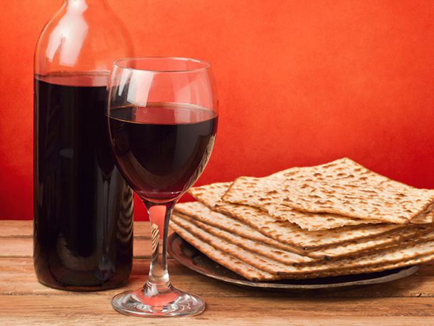 A glass of wine and a bottle of wine sitting next to a plate of matzoh.
