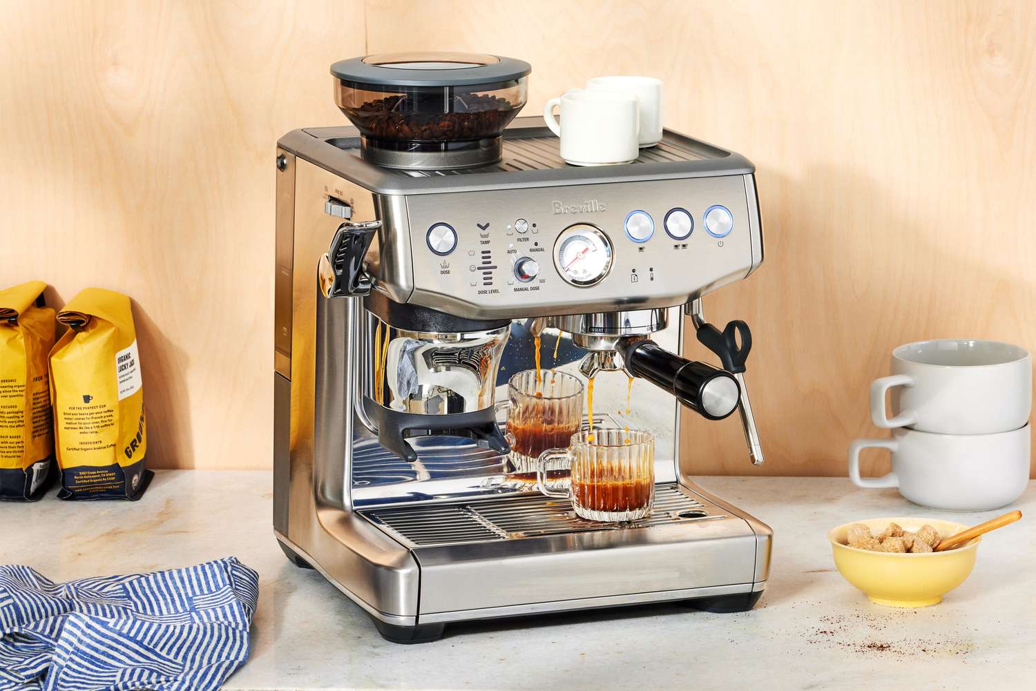 The Breville Barista Express Impress brewing coffee into a glass cup on a white marble countertop 