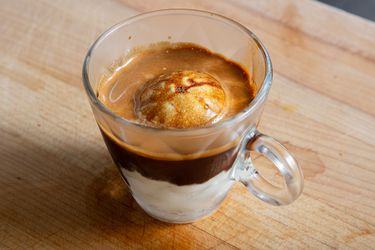 A transparent glass cup containing affogato, an espresso-based dessert with a scoop of vanilla ice cream