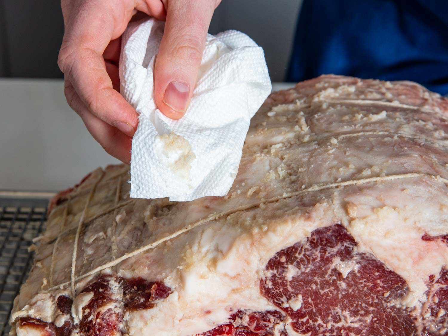 Blotting the surface of a prime rib with paper towel. 
