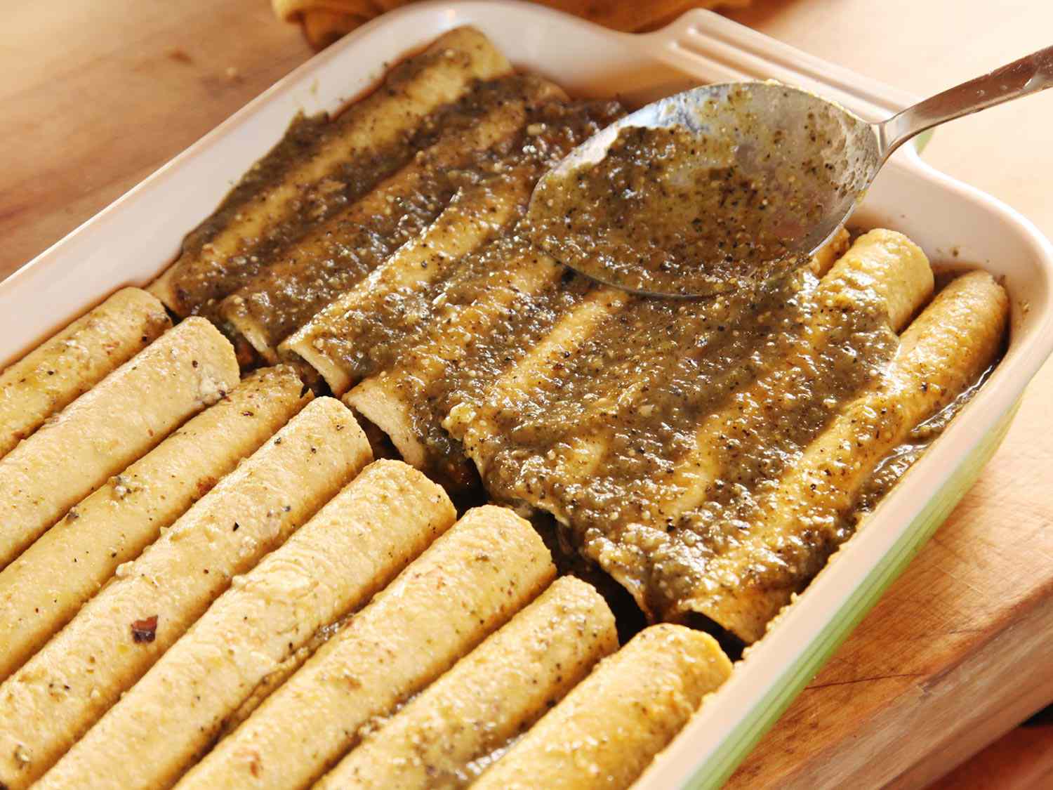 Sauce is spooned over the tortillas rolled up in baking dish.