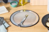 the le creuset splatter screen on a countertop with the handle folded 