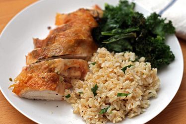 A plate of roasted chicken breast with crispy skin with brown rice and kale salad.
