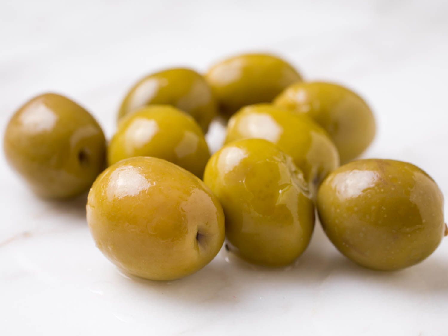 Closeup of shiny, plump, green olives on marble surface