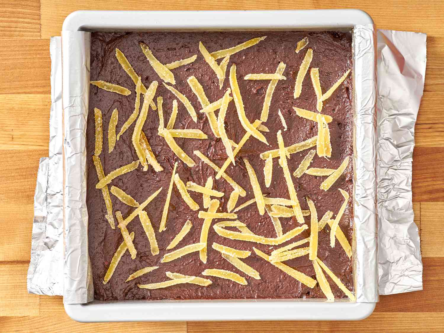 Brownie batter fills an aluminum-lined baking pan.