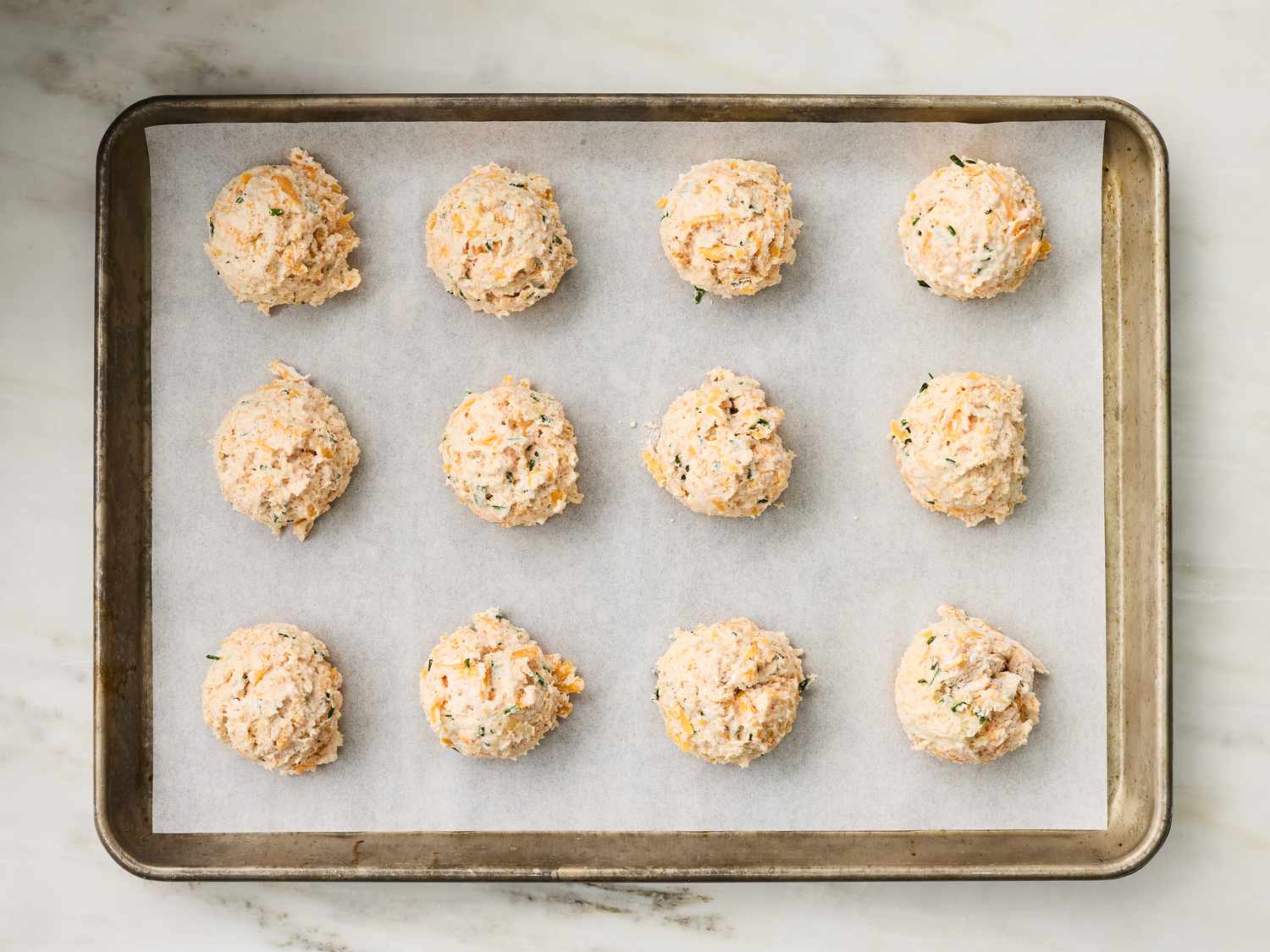 Twelve unbaked cheddar biscuits on a baking sheet lined with parchment paper