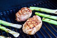 Two grilled Butcherbox meat cuts beside charred green onions on a barbecue grill
