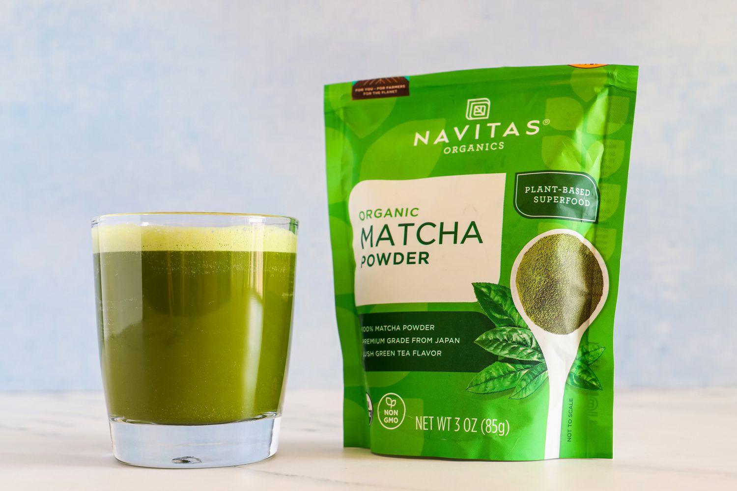 A bag of matcha powder labeled Navitas Organics and a glass of prepared matcha on a light surface