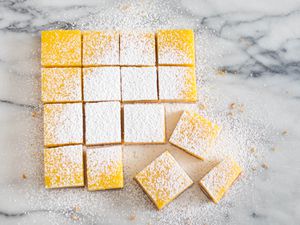 Overhead image showing sliced lemon bar squares topped with powdered sugar on a marble countertop.