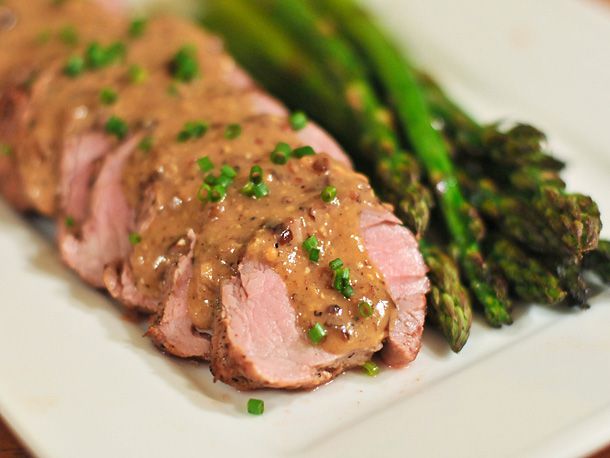 Sliced pork tenderloin topped with a mustard pan sauce and chives, alongside asparagus.