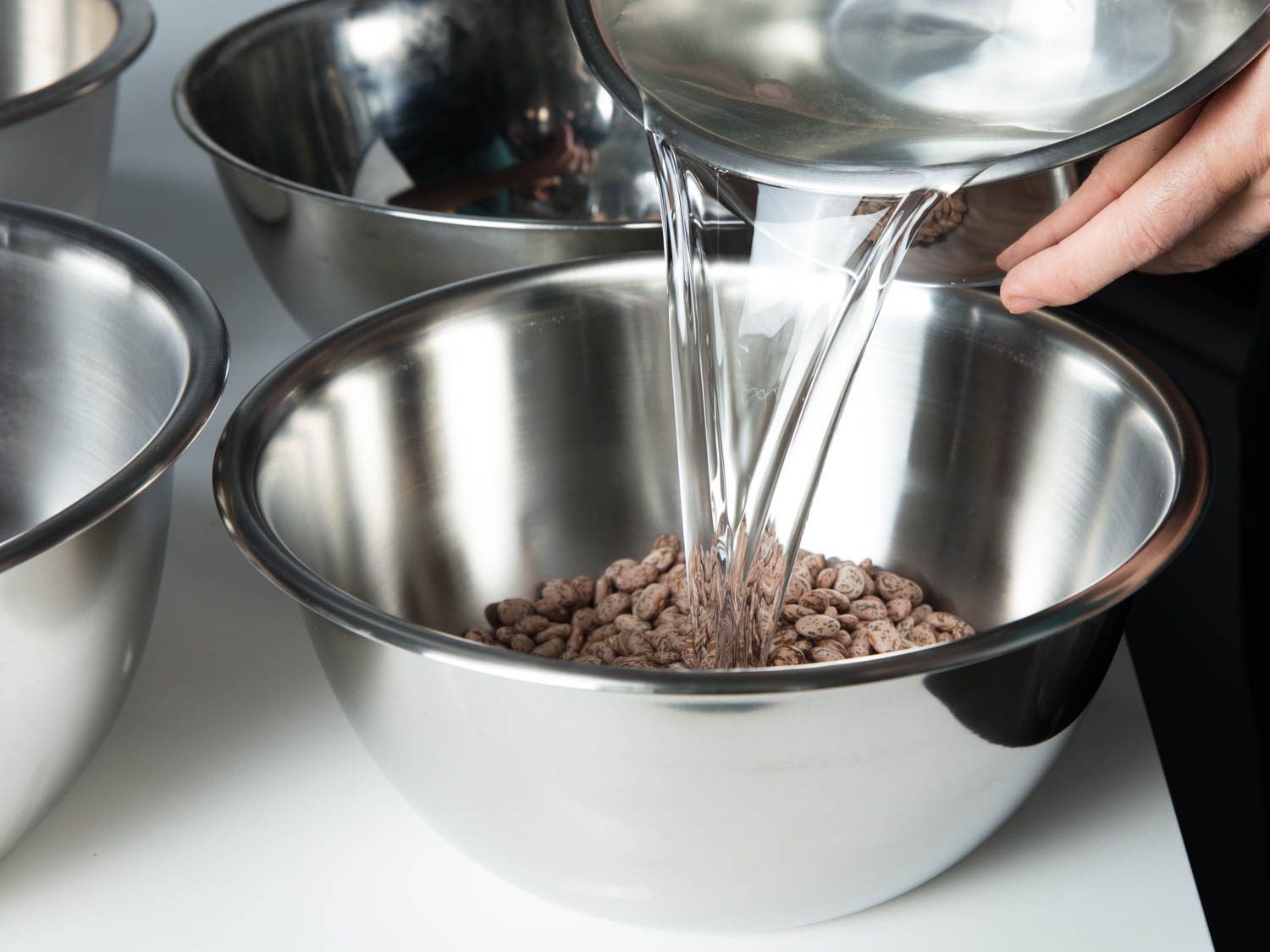 Pouring water into a large bowl filled with dried beans for soaking.