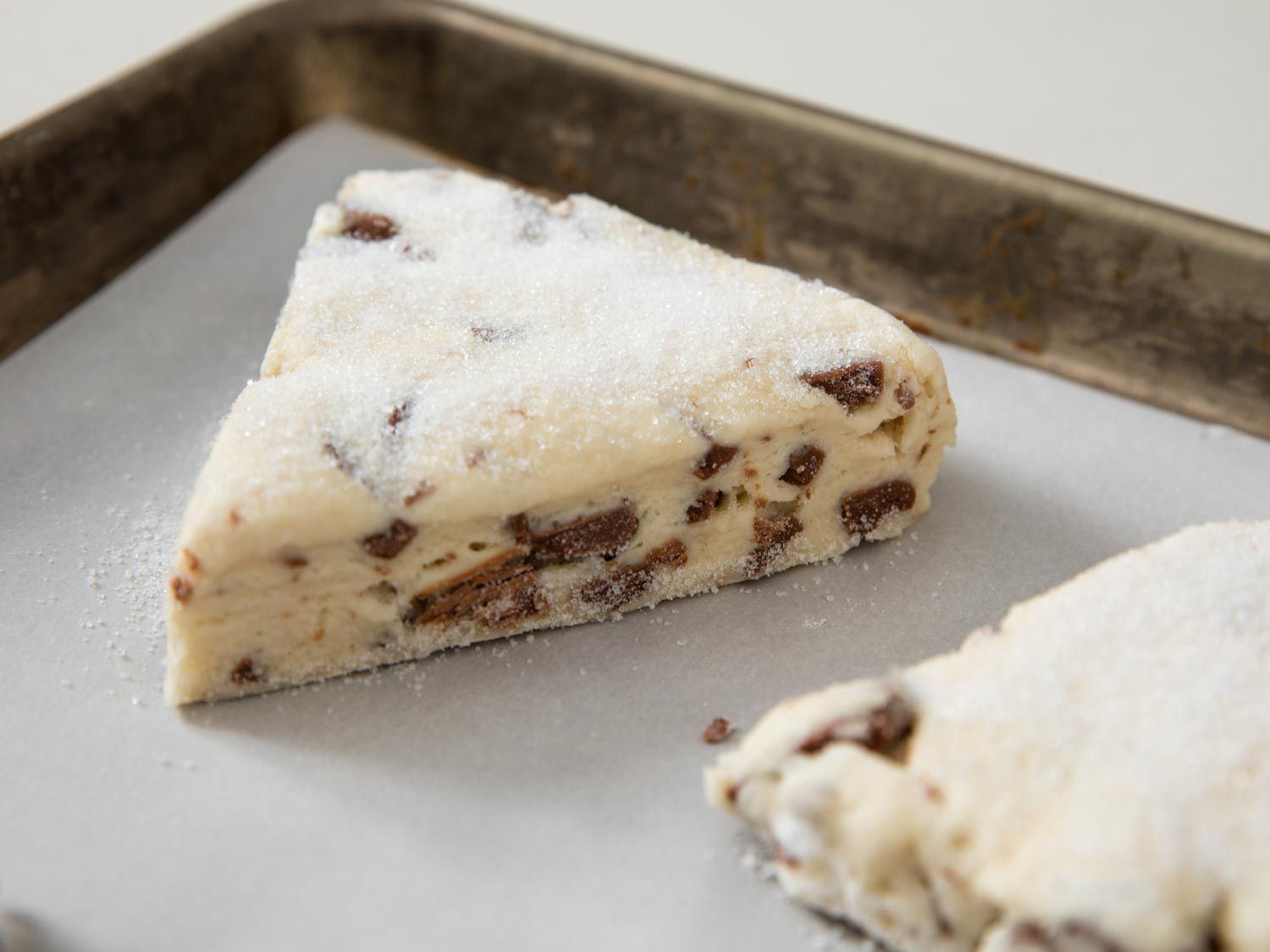 Wedges of unbaked chocolate chip scones on a parchment-lined baking sheet.