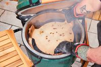 A person places a pizza stone inside the Big Green Egg Large Charcoal Kamado Grill and Smoker