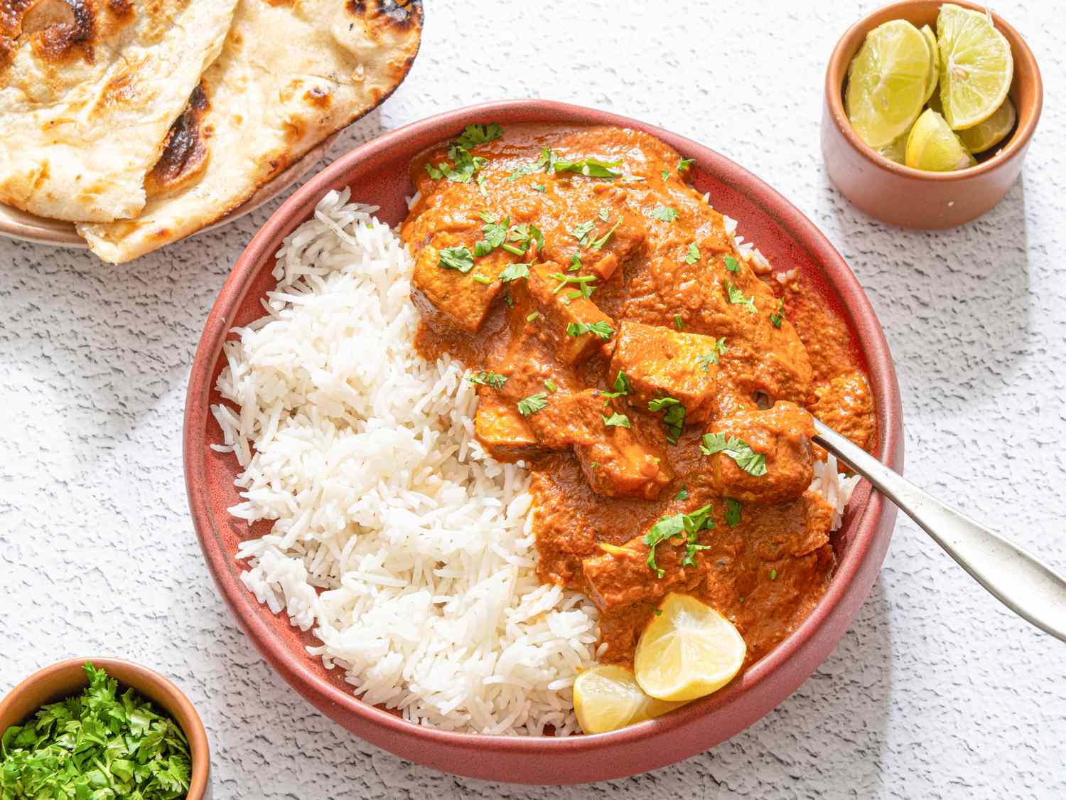 A plate of tofu tikka masala served with rice garnished with cilantro and lime