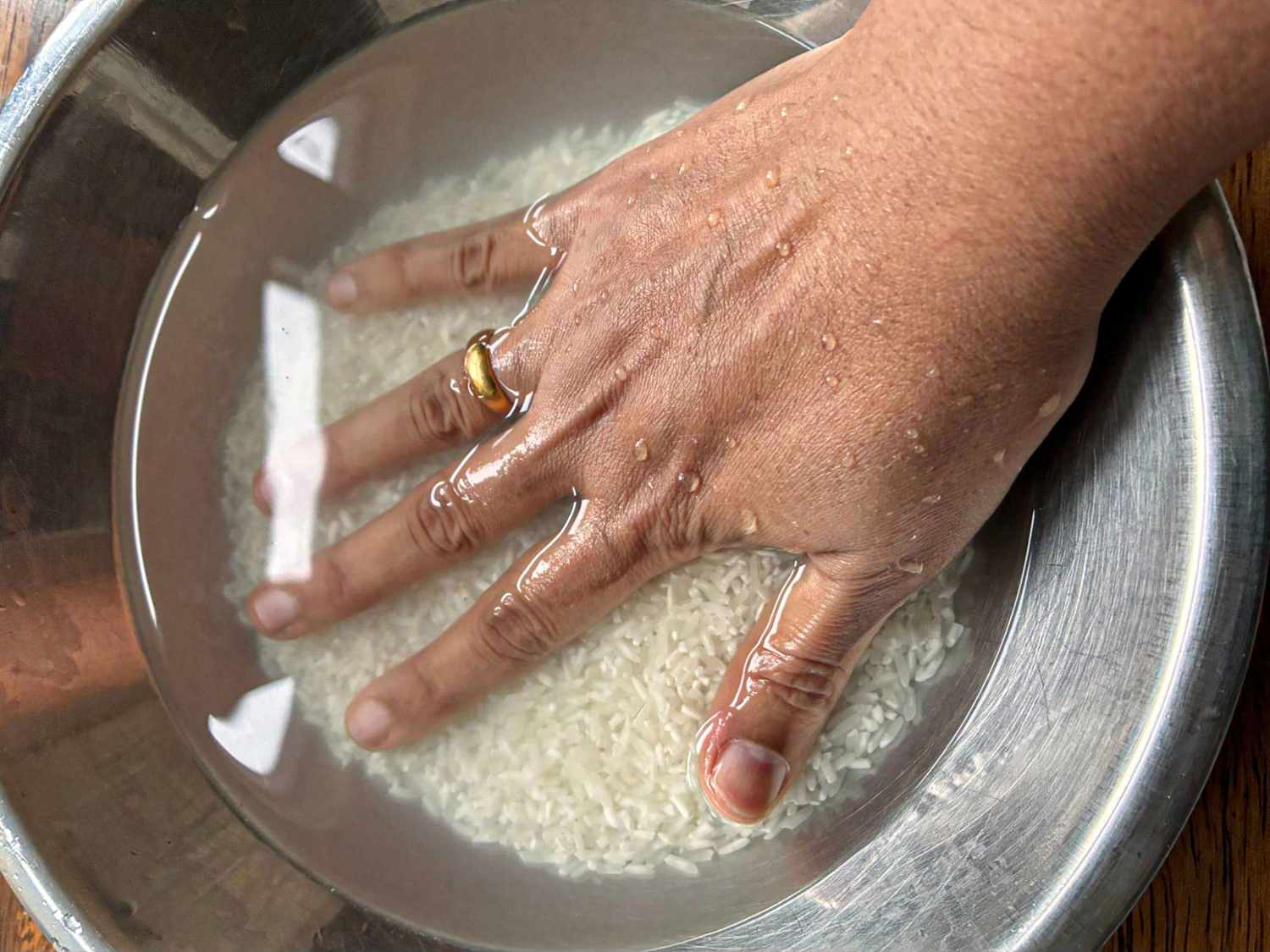 A hand rinsing rice in a bowl of water rings visible on fingers