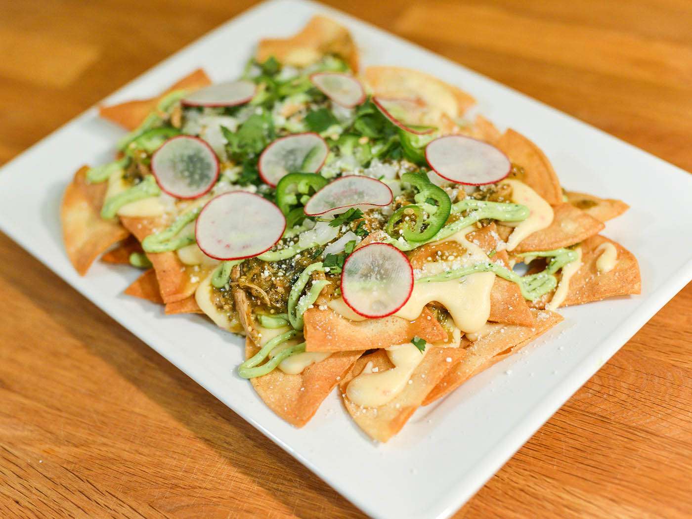 A platter of assembled green chile chicken nachos on a wooden surface